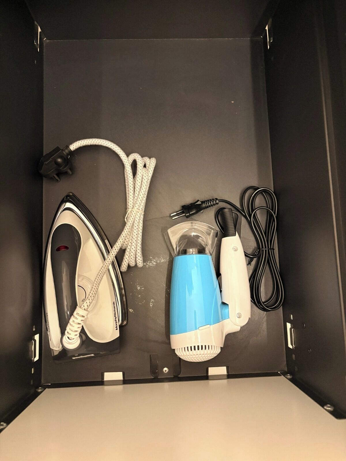 A storage box with a hairdryer, a blue and white electric shaver, and a black and white power cord.