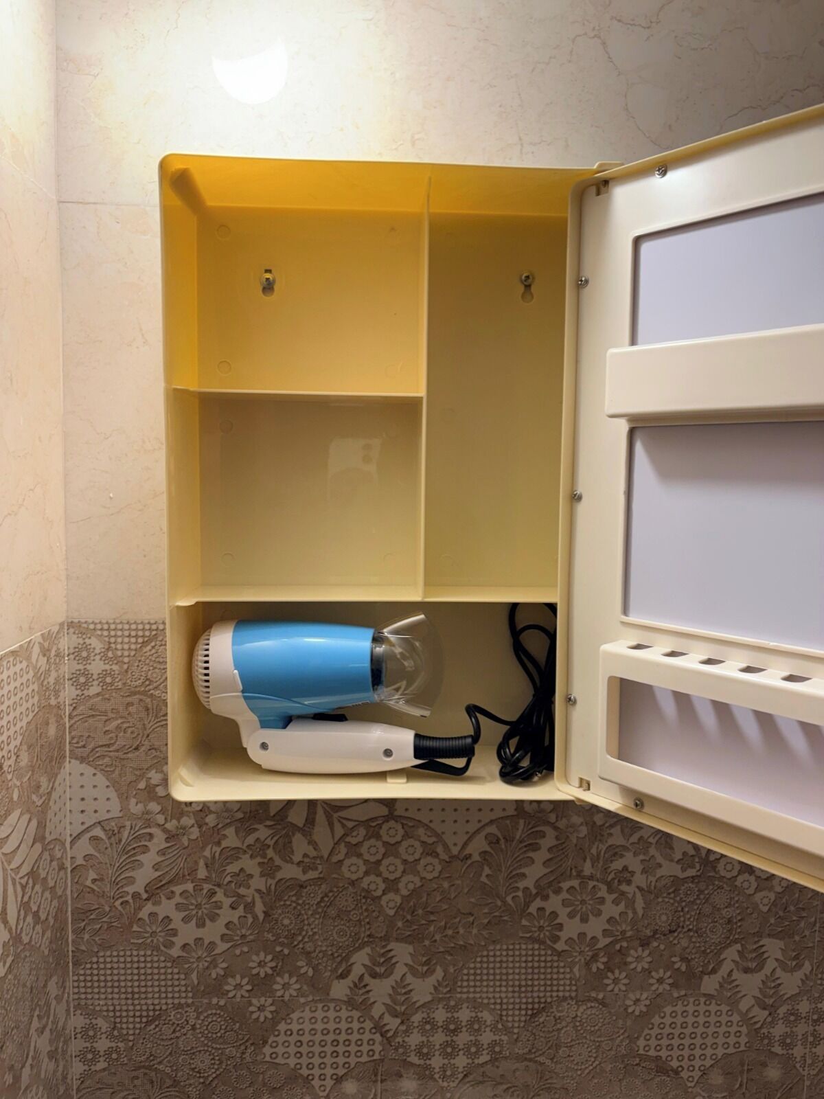 A bathroom with a yellow cabinet containing a blue hairdryer and a white mirror.