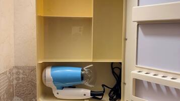 A bathroom with a yellow cabinet containing a blue hairdryer and a white mirror.