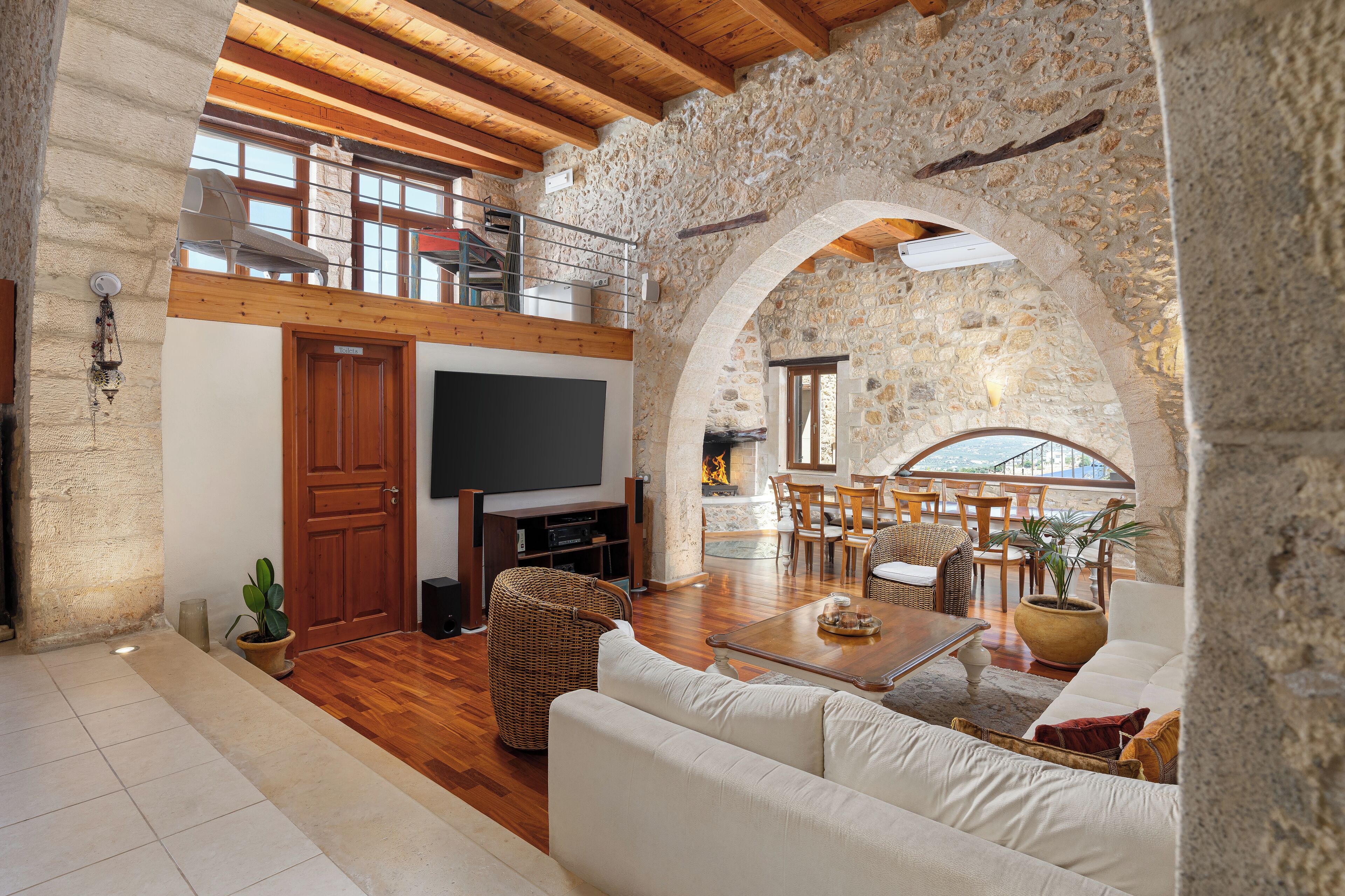 A spacious living area with a stone wall, wooden beams, a flat-screen TV, a dining set, and a cozy seating area.