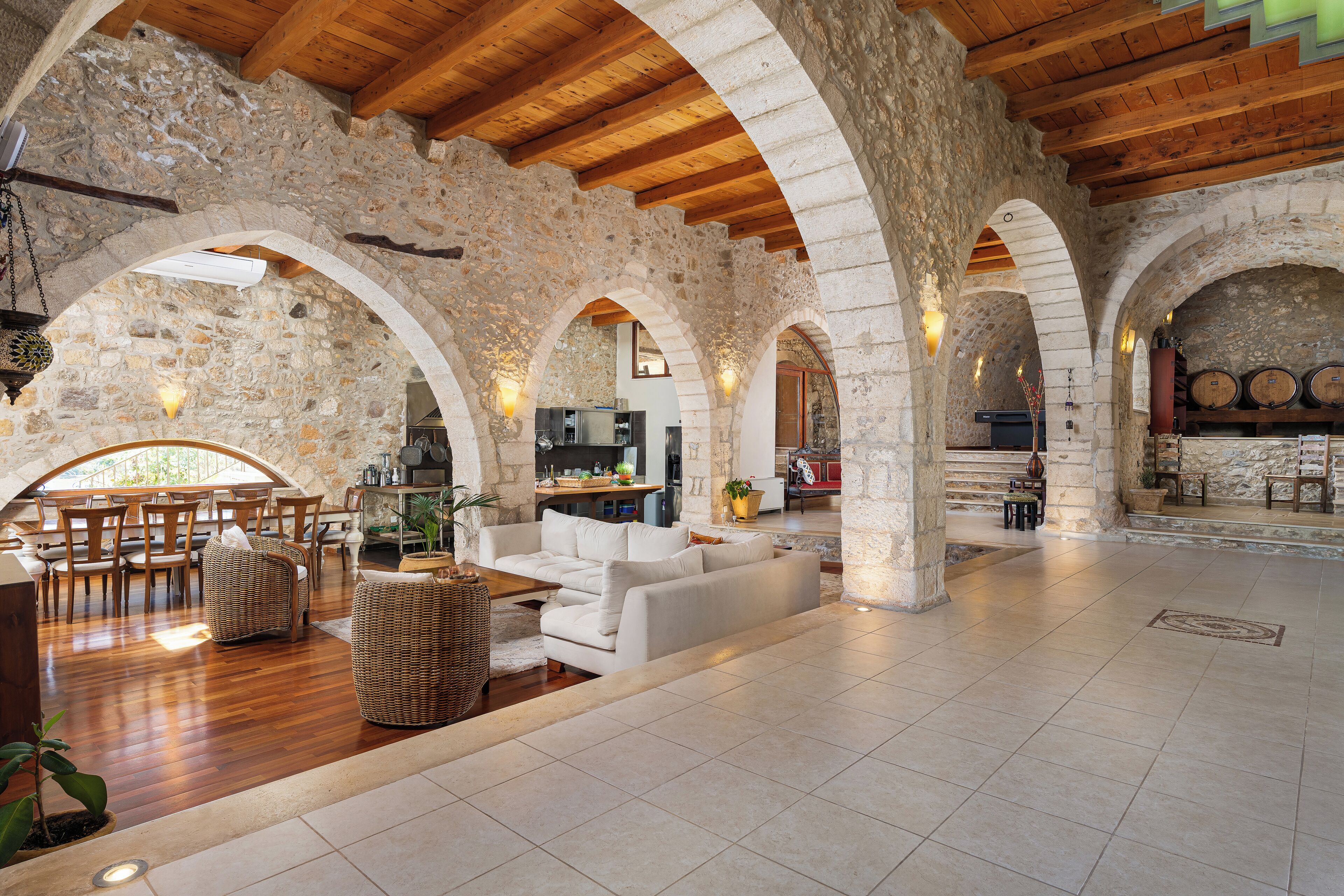 A spacious interior with stone walls, wooden beams, and a dining area with chairs and a table.