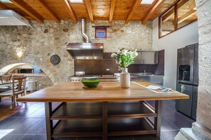 A kitchen with a stone wall, wooden ceiling, and modern appliances. - Candice Luxurious Historic Villa, Rentado Vacation Rental Management (Rethymno)