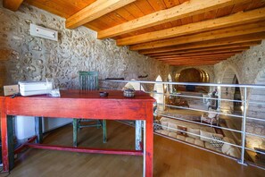 A rustic room with a stone wall, wooden ceiling beams, a red table, and a balcony railing. - Candice Luxurious Historic Villa, Rentado Vacation Rental Management (Rethymno)