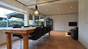 A spacious dining area with a long wooden table and black chairs, a TV mounted on the wall, and a large window providing natural light. - Holiday Home With Infrared Sauna in Callantsoog (Callantsoog)