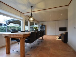 Ein geräumiger Essbereich mit einem langen Holztisch und schwarzen Stühlen, einem an der Wand befestigten Fernseher und einem großen Fenster, das für natürliches Licht sorgt.