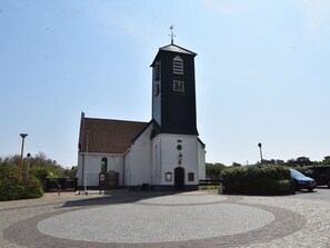 A church with a clock tower, a cobblestone courtyard, and a car parked nearby. - Holiday Home With Infrared Sauna in Callantsoog (Callantsoog)
