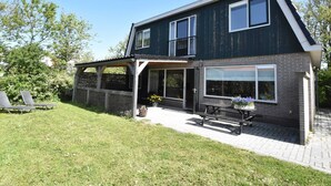 A two-story house with a balcony, a covered porch, and a paved driveway. - Holiday Home With Infrared Sauna in Callantsoog (Callantsoog)