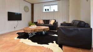 A living room with a flat-screen TV, a wooden coffee table, a black leather sofa, and a cowhide rug. - Holiday Home With Infrared Sauna in Callantsoog (Callantsoog)