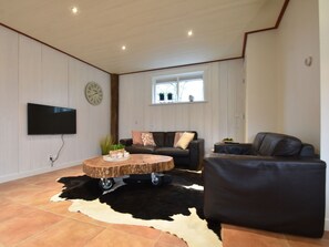 Ein Wohnzimmer mit Flachbildfernseher, Couchtisch aus Holz, schwarzem Ledersofa und einem Teppich aus Rindsleder.