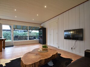 A spacious living area with a large window, a flat-screen TV mounted on the wall, and a wooden coffee table. - Holiday Home With Infrared Sauna in Callantsoog (Callantsoog)