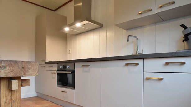 A kitchen with white cabinets, a black countertop, and a wooden accent piece. - Holiday Home With Infrared Sauna in Callantsoog (Callantsoog)