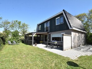 A two-story house with a covered patio, a lawn, and a garden area. - Holiday Home With Infrared Sauna in Callantsoog (Callantsoog)