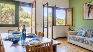 Un coin repas avec une table dressée pour quatre personnes, un canapé et une vue sur la verdure grâce à de grandes fenêtres.