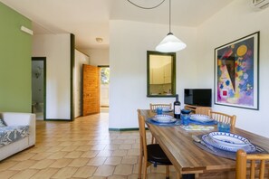 Un coin repas avec une table en bois dressée pour quatre personnes, des chaises, une suspension et un grand tableau abstrait accroché au mur.