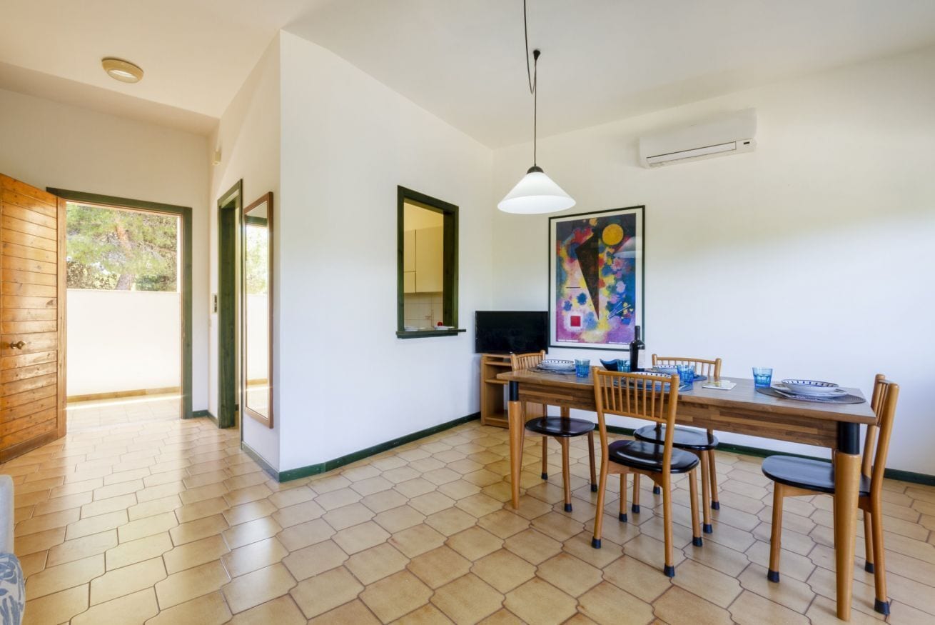A dining area with a wooden table and chairs, a pendant light, and a painting on the wall.
