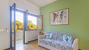 Une pièce comprenant un canapé, un tableau abstrait encadré et une porte donnant sur un balcon.