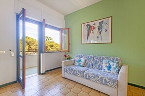 A room with a sofa, a framed abstract painting, and a door leading to a balcony. - A comfortable apartment with a balcony that sleeps up to four people, located within the Campoverde Residence in Vernole—set in a Mediterranean pine forest between San Cataldo and the Le Cesine Nature Reserve. The property is just a short distance from (Campo Verde)