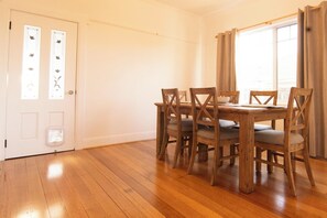 Ein Essbereich mit einem Holztisch und -stühlen, einer weißen Tür mit dekorativen Glasfeldern und einem Fenster mit Vorhängen.