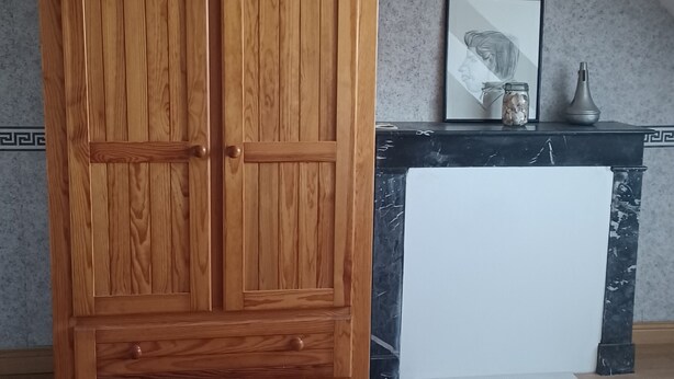 Une armoire en bois, une cheminée en marbre, un tableau encadré et un petit vase posé sur le manteau de la cheminée.