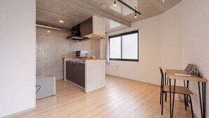 Una cuina moderna amb una illa central, una zona de menjador amb taula i cadires, i un gran finestral que aporta llum natural.