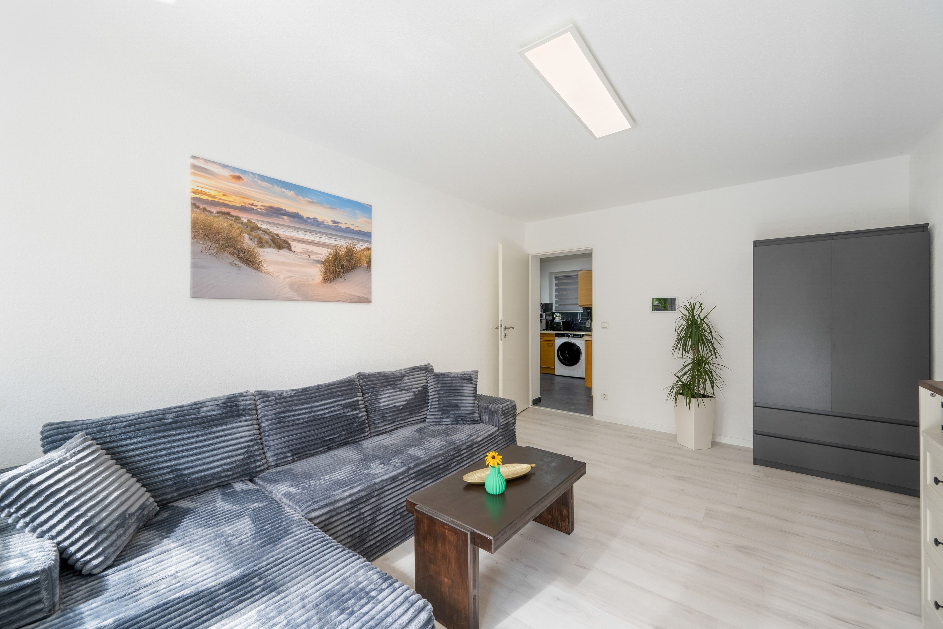 Ein modernes Wohnzimmer mit einer Couch, einem Couchtisch und einem Bild von einer Strandlandschaft.