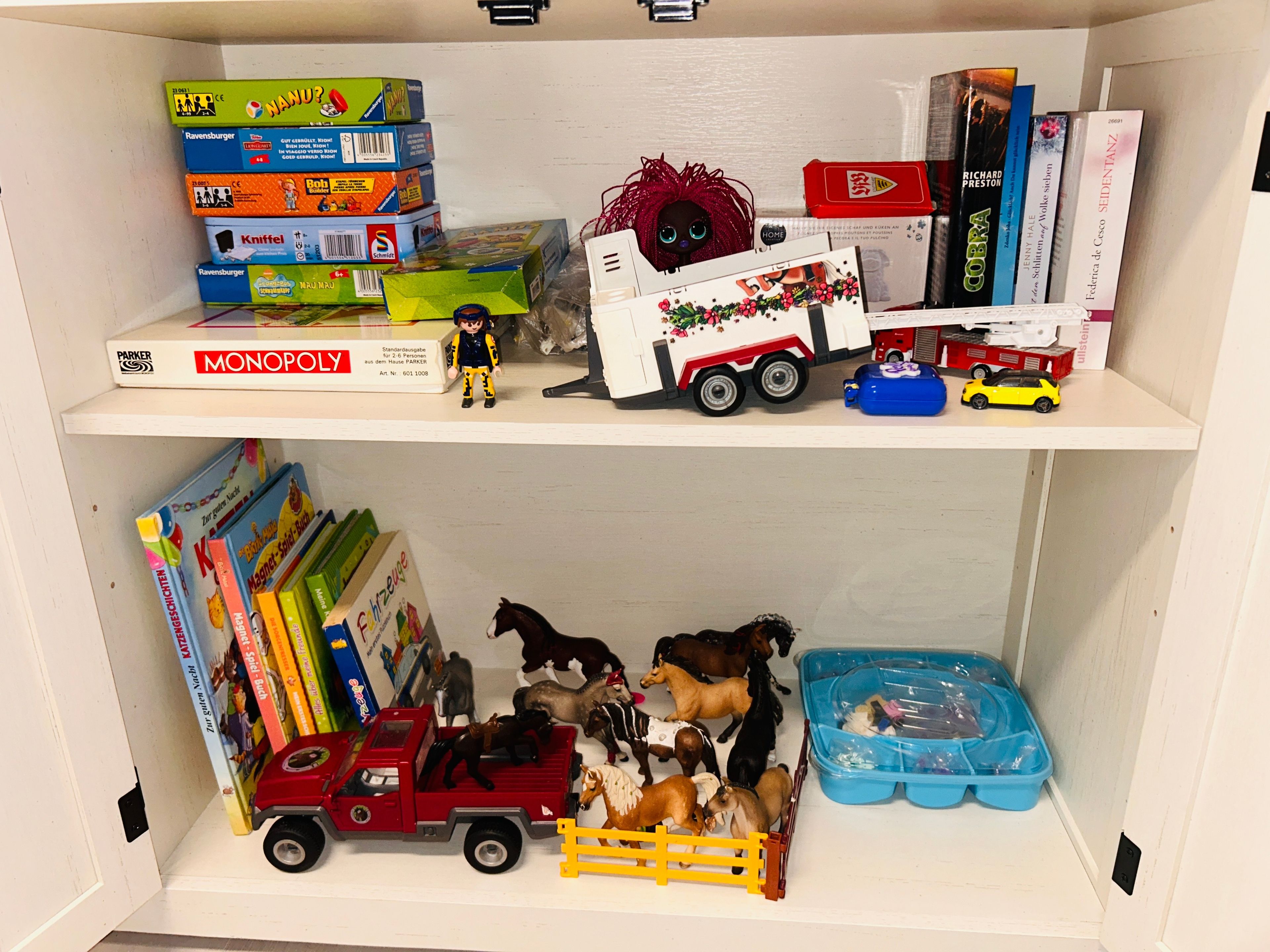A shelf with various board games, a doll, and toy vehicles.