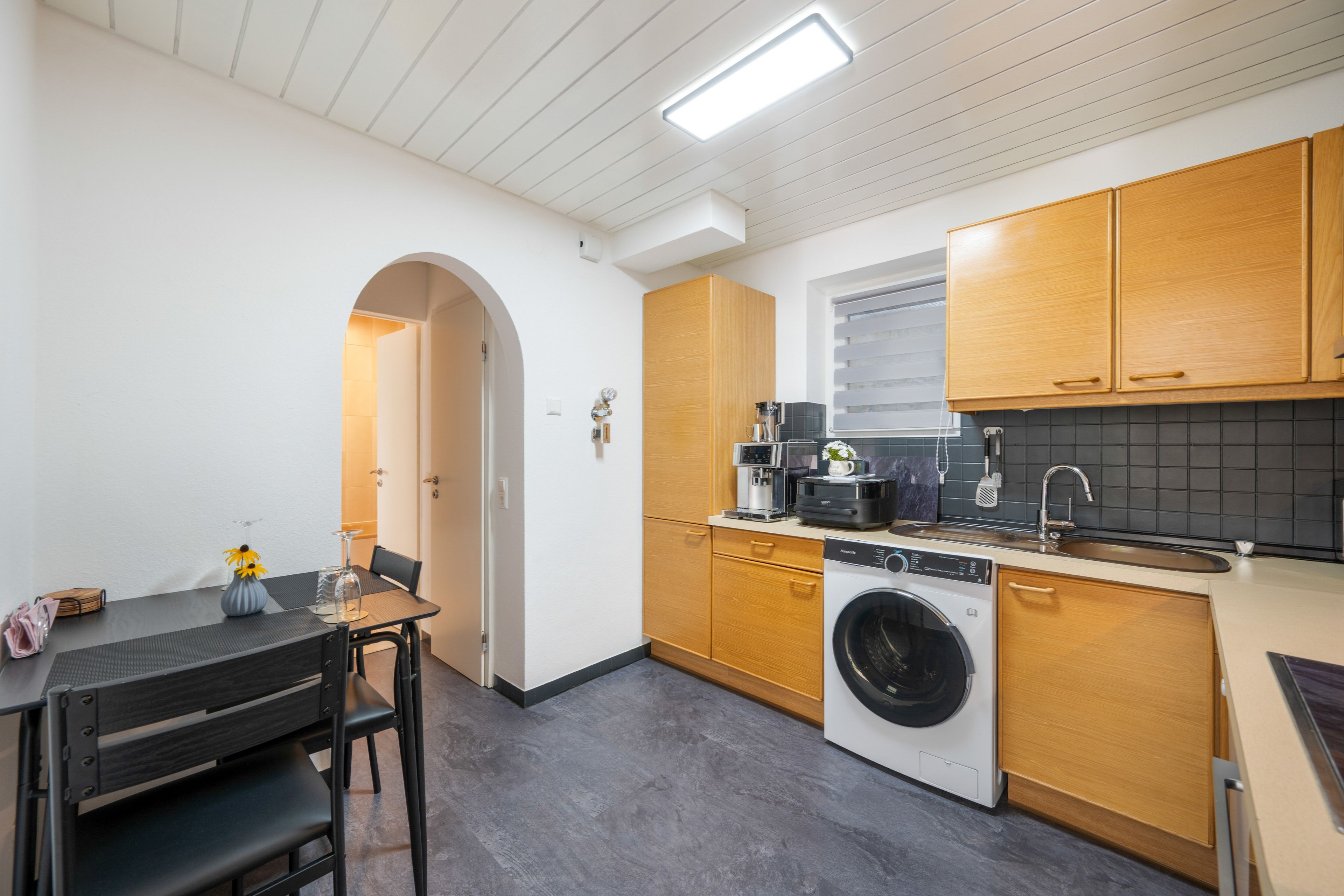 A compact kitchen with a washing machine, a coffee maker, and a dining area with a table and chairs.