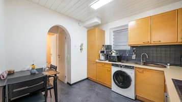 Cocina compacta con lavadora, cafetera y comedor con mesa y sillas.