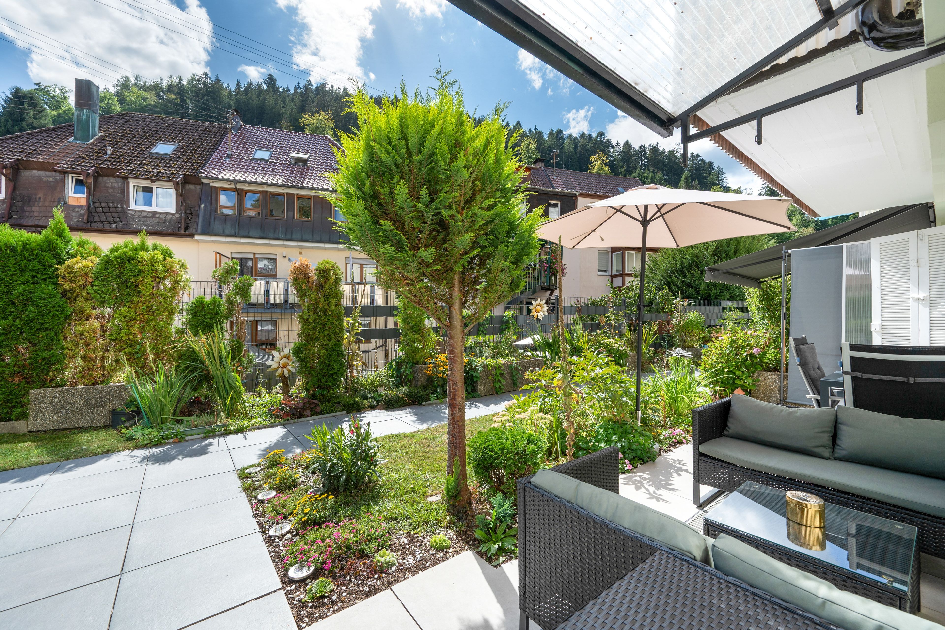 A patio area with outdoor furniture, a garden with various plants, and a view of residential buildings in the background.