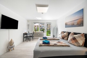 Ein modernes Zimmer mit einem Bett, einem Flachbildfernseher, einem Schreibtisch mit Stuhl und Blick durch eine Glastür auf einen Außenbereich.