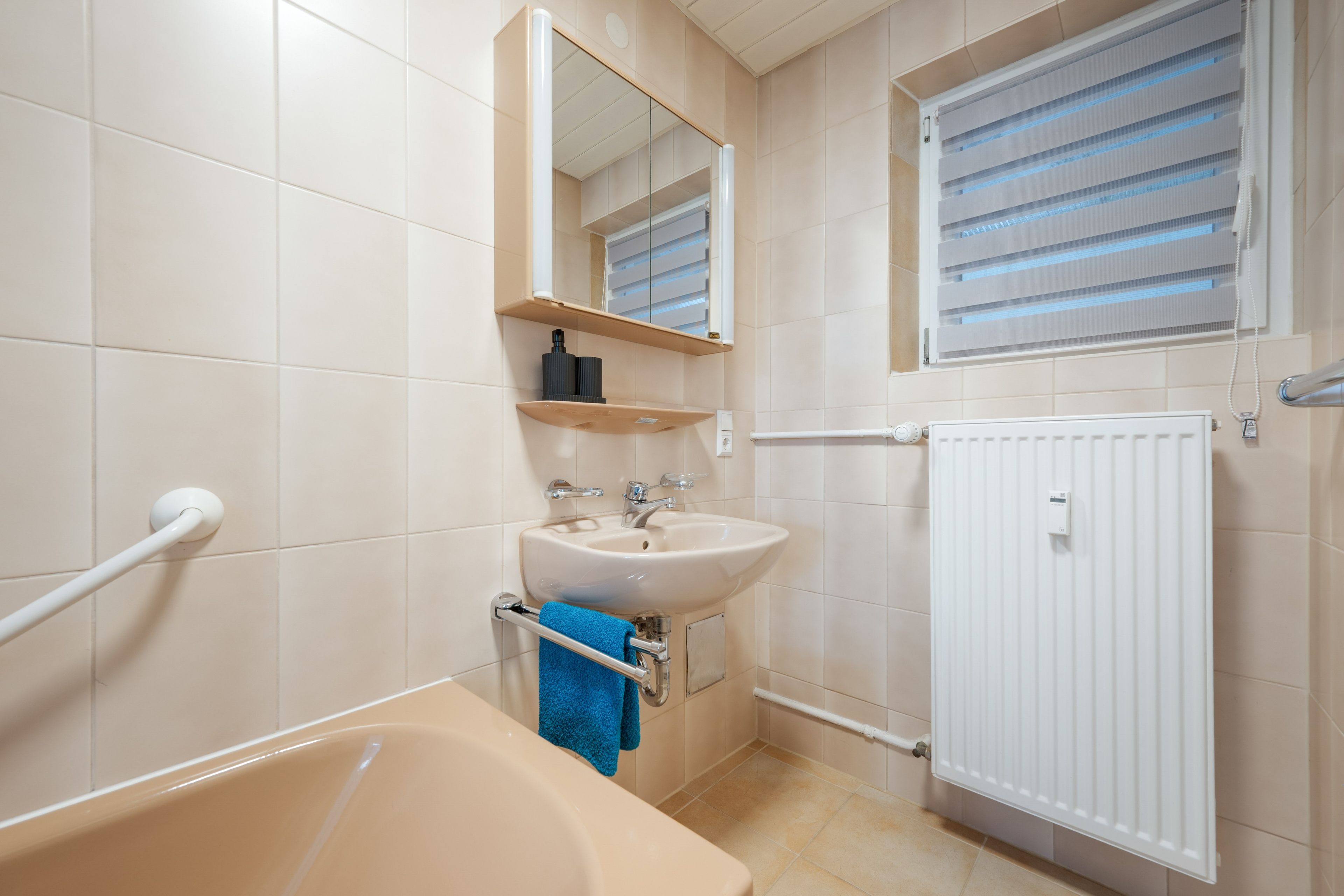 Ein Badezimmer mit einer Badewanne, einem Waschbecken, einem Spiegel, einem Handtuchhalter und einer Heizung.