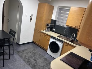 Una cocina compacta con lavadora, cafetera y lavabo.