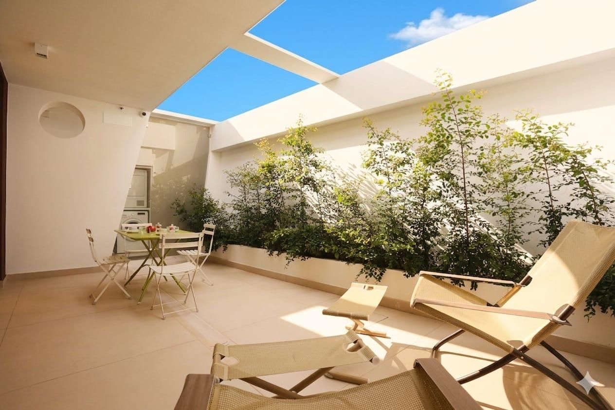 Eine moderne Terrassengruppe im Freien mit Esstisch und Lounge-Stühlen, umgeben von Pflanzen und blauem Himmel.