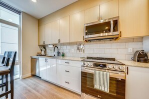A modern kitchen with wooden cabinets, a stainless steel microwave, an oven, and a countertop with various kitchen items. - Rooftop Brews & Mtn Views: Central Seattle Gem (Seattle)