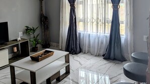 Un salon moderne avec un sol en marbre, un canapé blanc, une table basse, un téléviseur et un luminaire décoratif au plafond.
