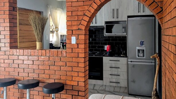 Un salon avec un canapé, un mur en briques, une cuisine avec un réfrigérateur et un coin repas avec une table et des chaises.