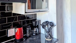 Une cuisine avec des meubles blancs, un four à micro-ondes, une machine à café et une bouilloire.