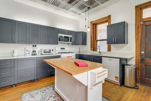 A modern kitchen with grey cabinets, a wooden island, and a stainless steel trash can. - Historic Queen Anne Omaha Home in Field Club (Omaha)