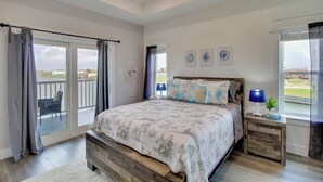 Une chambre à coucher avec un grand lit, une table de chevet en bois, une fenêtre avec des rideaux et une vue sur l’extérieur.