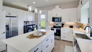 Une cuisine moderne avec des meubles blancs, des appareils en acier inoxydable et un îlot central.