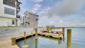 Une propriété située au bord de l’eau, dotée d’une jetée en bois, d’une promenade en béton et d’une grande maison avec de nombreux balcons.