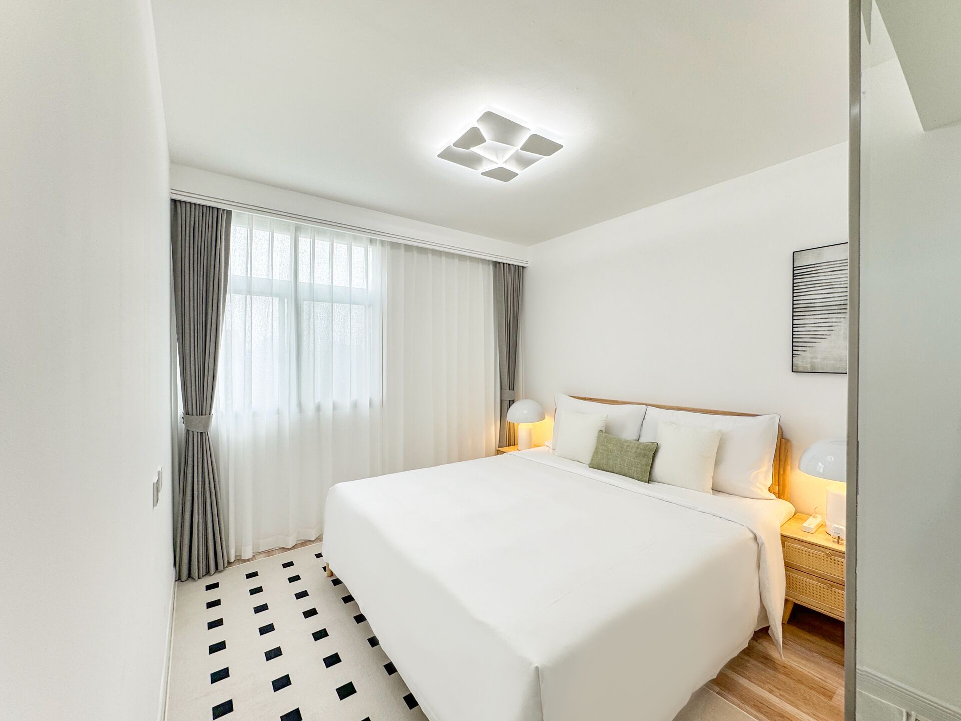 Habitación de hotel con una cama grande, una mesita de noche con lámpara, una ventana con cortinas y una lámpara en el techo.