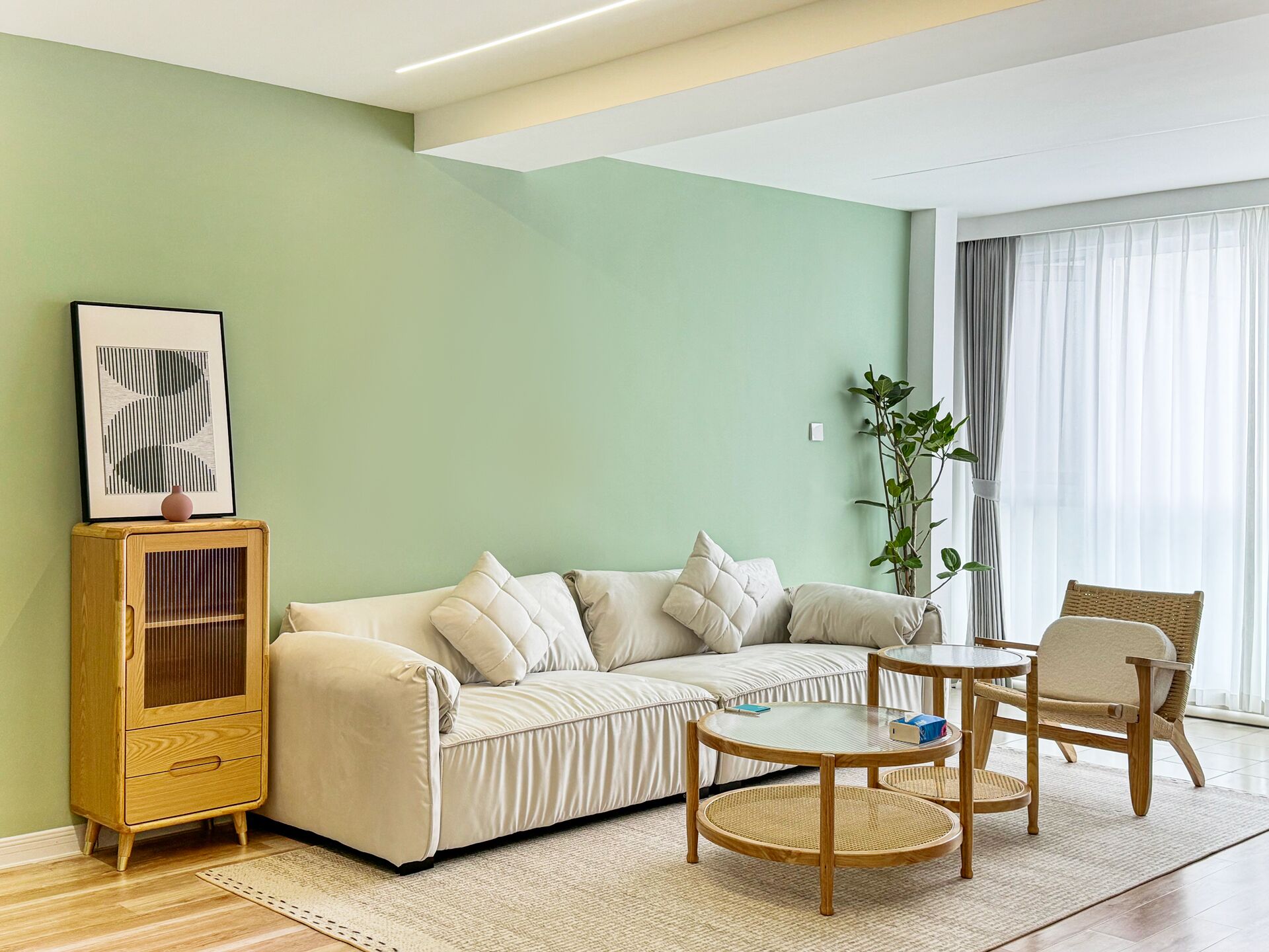 A living room with a sofa, two chairs, a small table, a cabinet, and a plant.