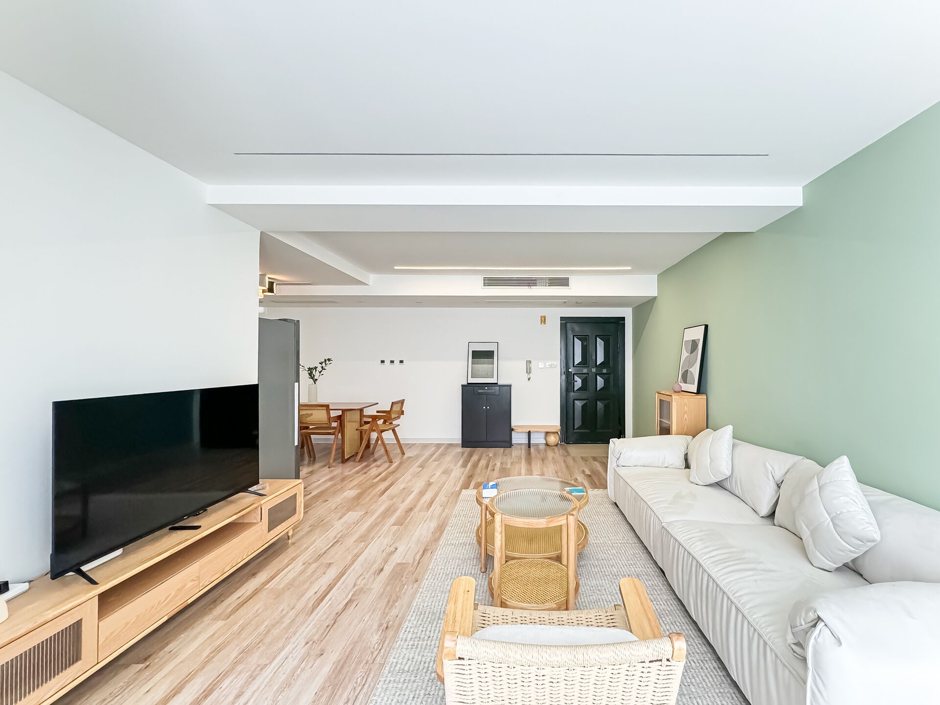Ein modernes Wohnzimmer mit Flachbildfernseher, Holzmöbeln, einem weißen Sofa und einem Essbereich im Hintergrund.