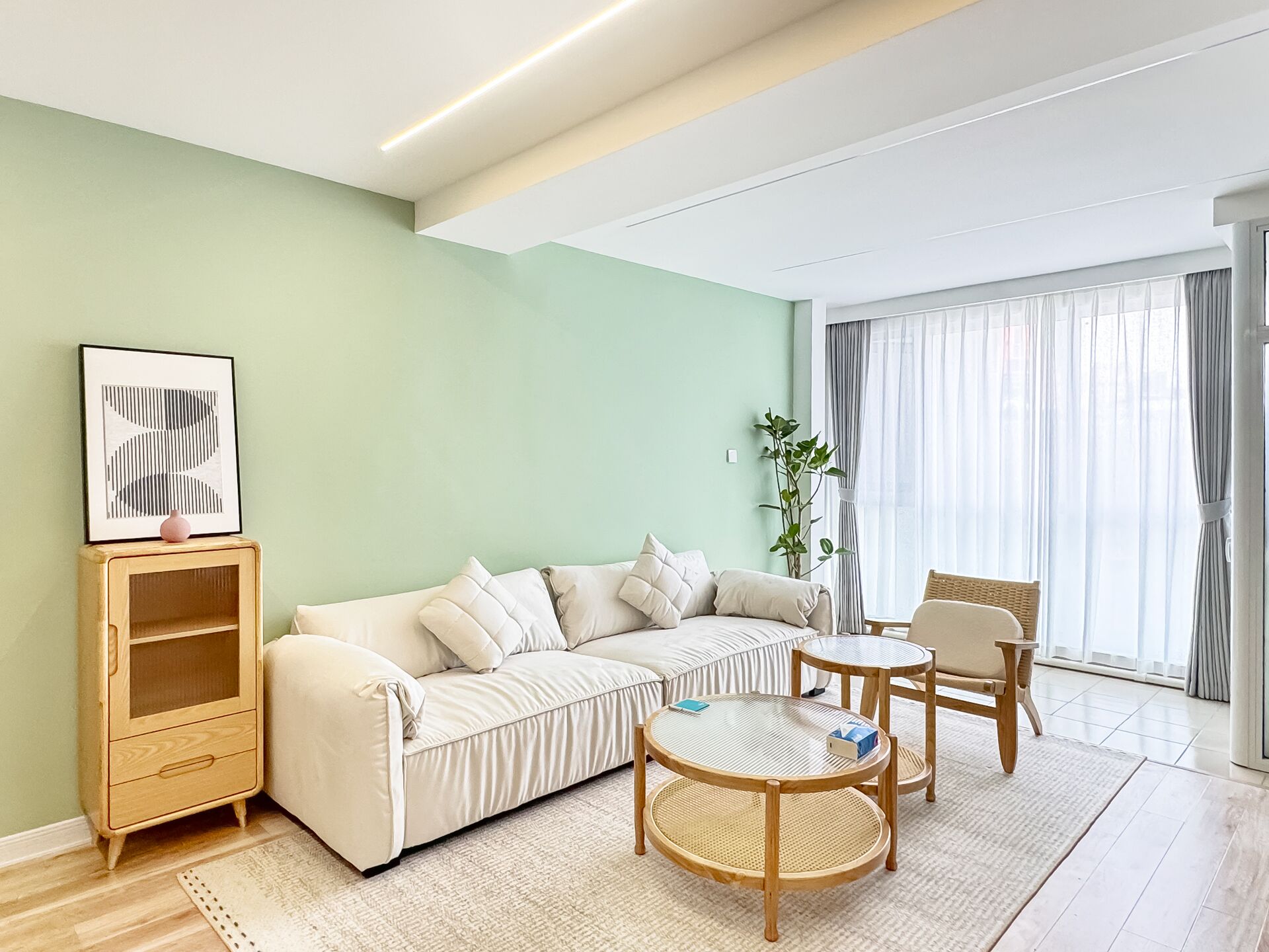 Una sala de estar moderna con un sofá, dos mesas redondas, un aparador y un ventanal con cortinas.