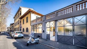 A street view with parked cars and a scooter, buildings with large windows, and a clear sky. - Giano Della Bella (Florence)