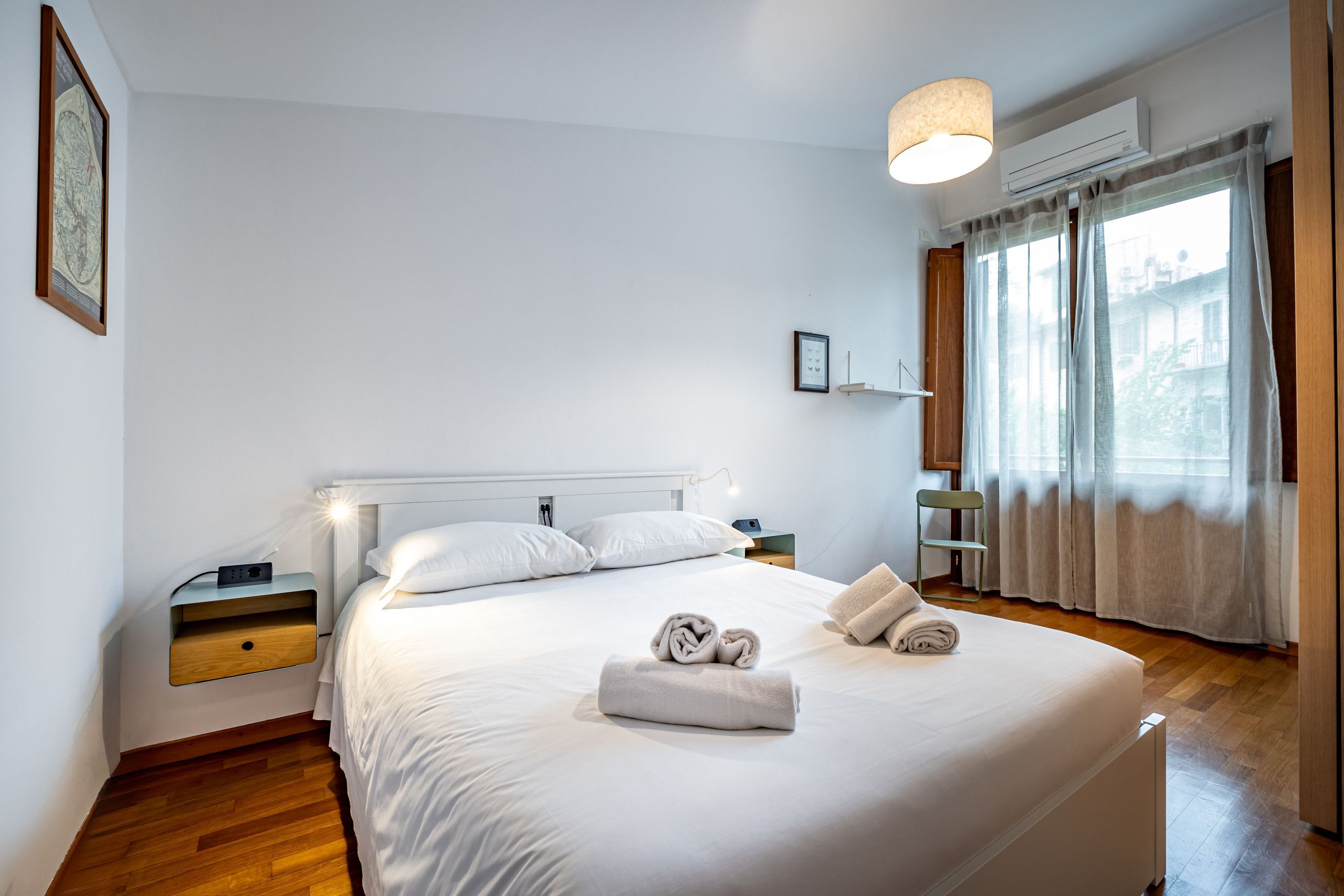 A neatly arranged bedroom with a large bed, bedside tables, a hanging light fixture, and a window with curtains.