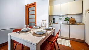 A compact kitchen with white cabinets, a wooden-framed window, and a dining area set with plates, glasses, and a woven placemat. - Giano Della Bella (Florence)