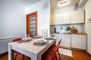 A compact kitchen with white cabinets, a wooden-framed window, and a dining area set with plates, glasses, and a woven placemat. - Giano Della Bella (Florence)