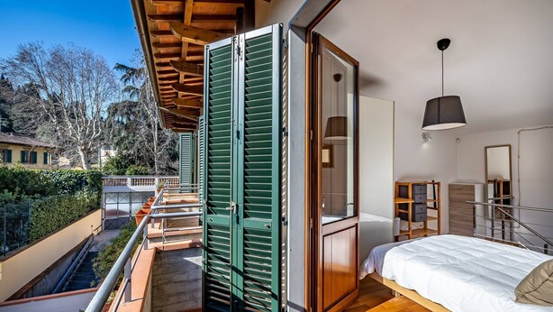 A bedroom with a bed, a wardrobe, and a balcony with green shutters. - Giano Della Bella (Florence)